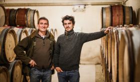 Laurent and Adrian Pillot in their wine cellar surrounded by barrels.