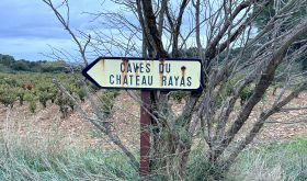 Sign pointing to Château Rayas winery, with vineyard in background.