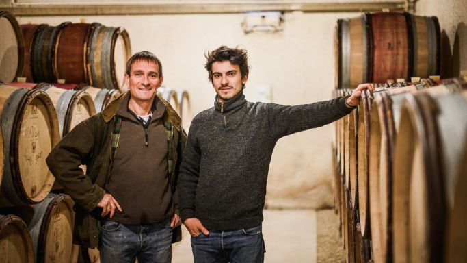 Laurent and Adrian Pillot in their wine cellar surrounded by barrels.