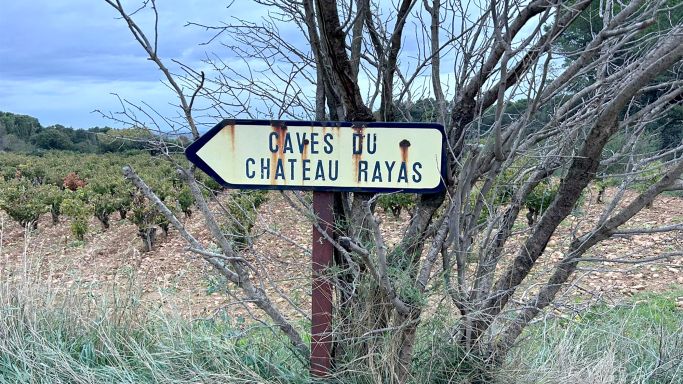 Sign pointing to Château Rayas winery, with vineyard in background.