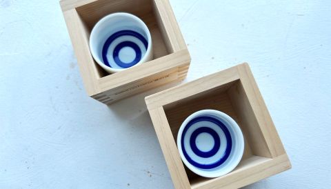 Blue-and-white bulls-eye ceramic sake cups in cedar boxes to catch overflow.
